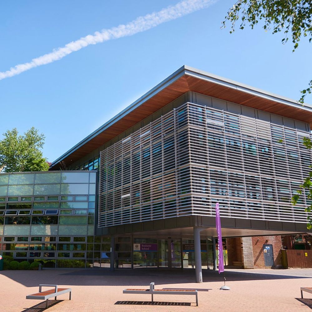 A building made from glass and metal against a backdrop of blue sky with tree leaves around the sides.