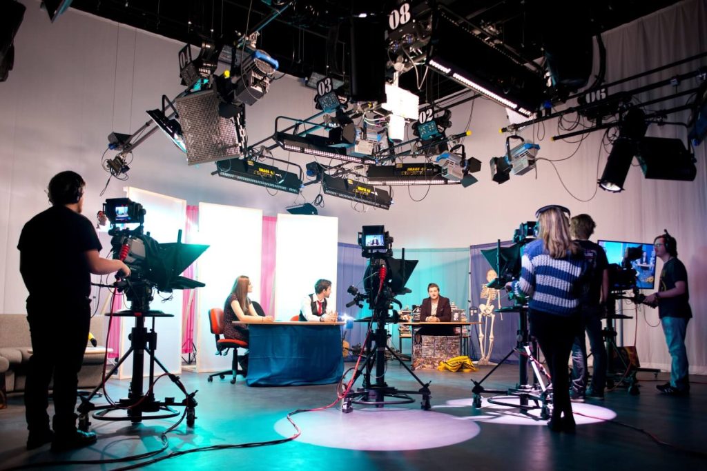 Students operate cameras and film presenters recording in the TV studio in Creative Edge.