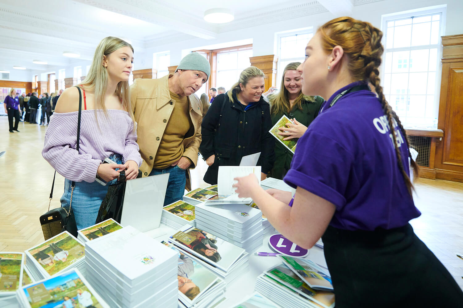 Visit us in-person or online - A student and her father speak to a member of the Open Day team at a stand in Sages Restaurant during an event.