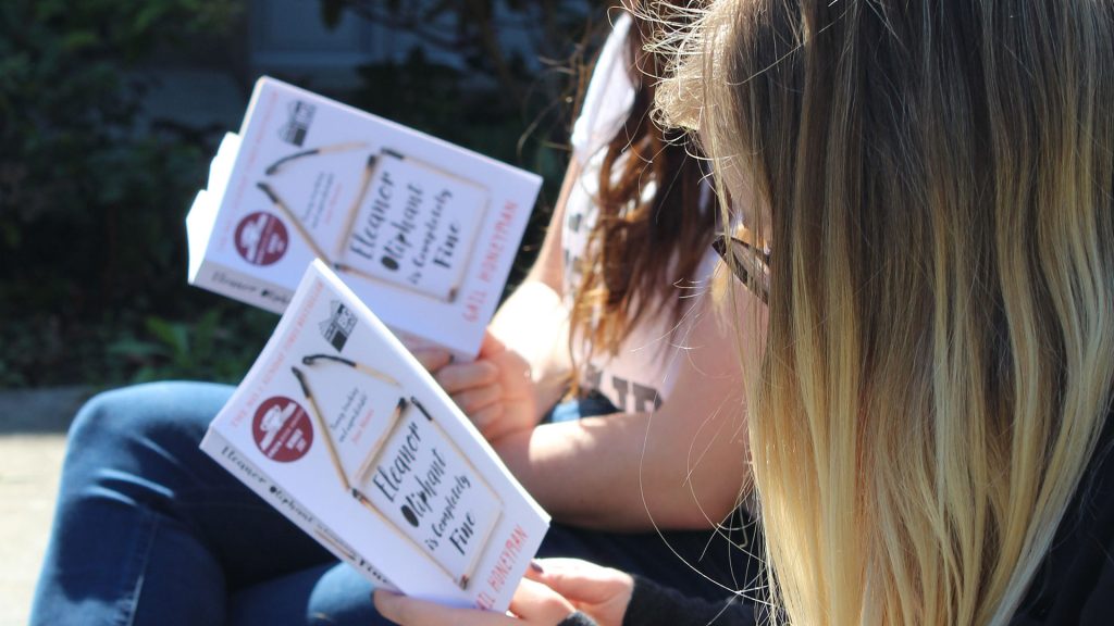 Two people sit side by side reading Eleanor Oliphant is Completely Fine 