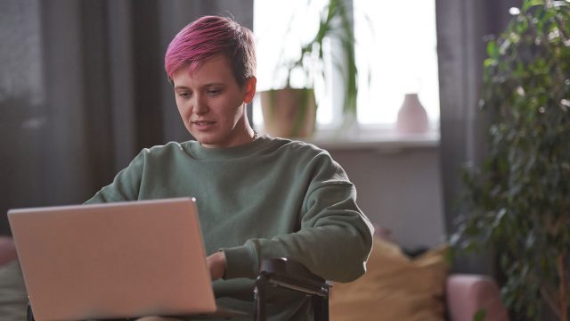 Young disabled woman sitting in wheelchair and typing on laptop computer