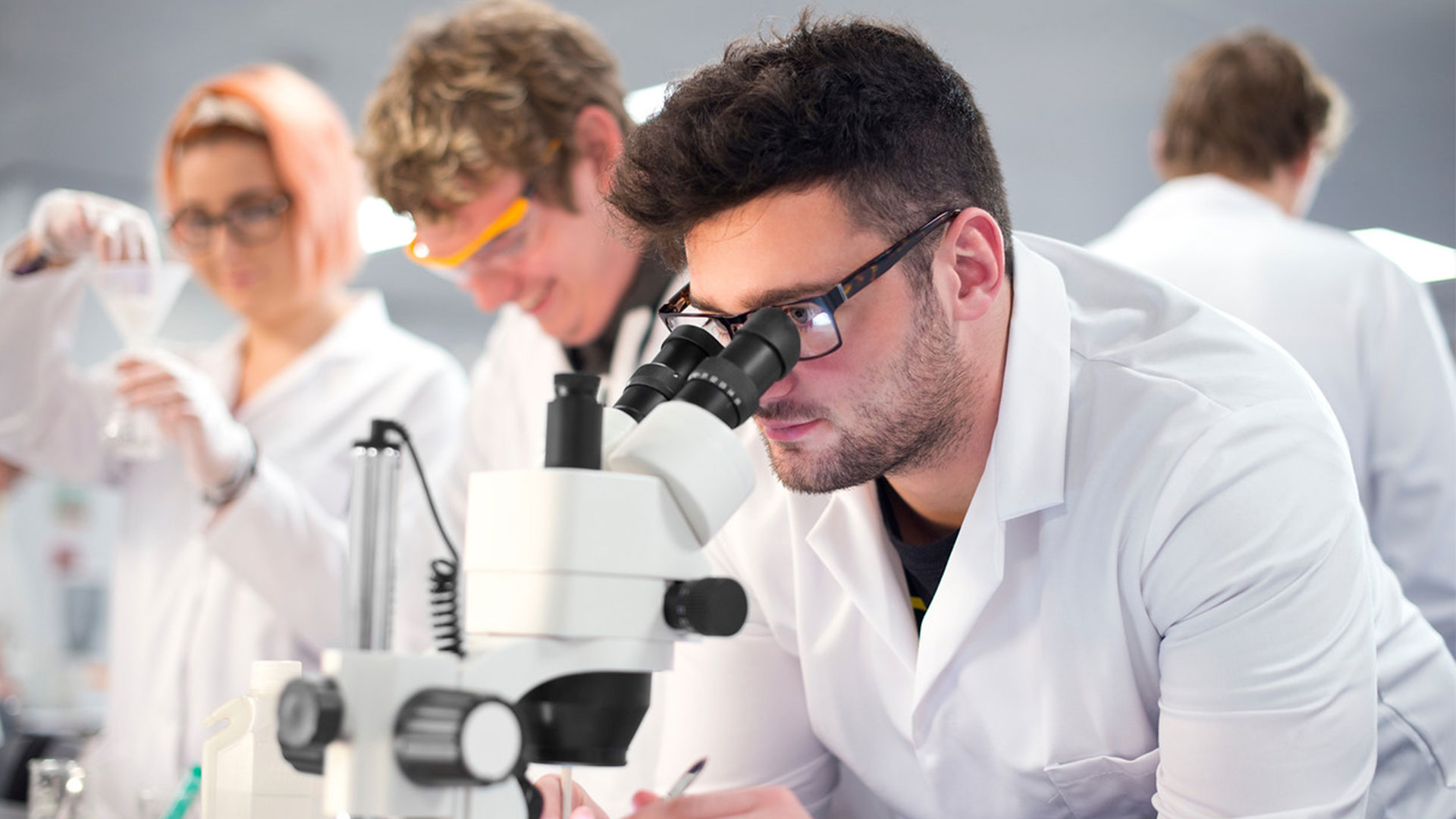 A student in white overalls looking down a microscope