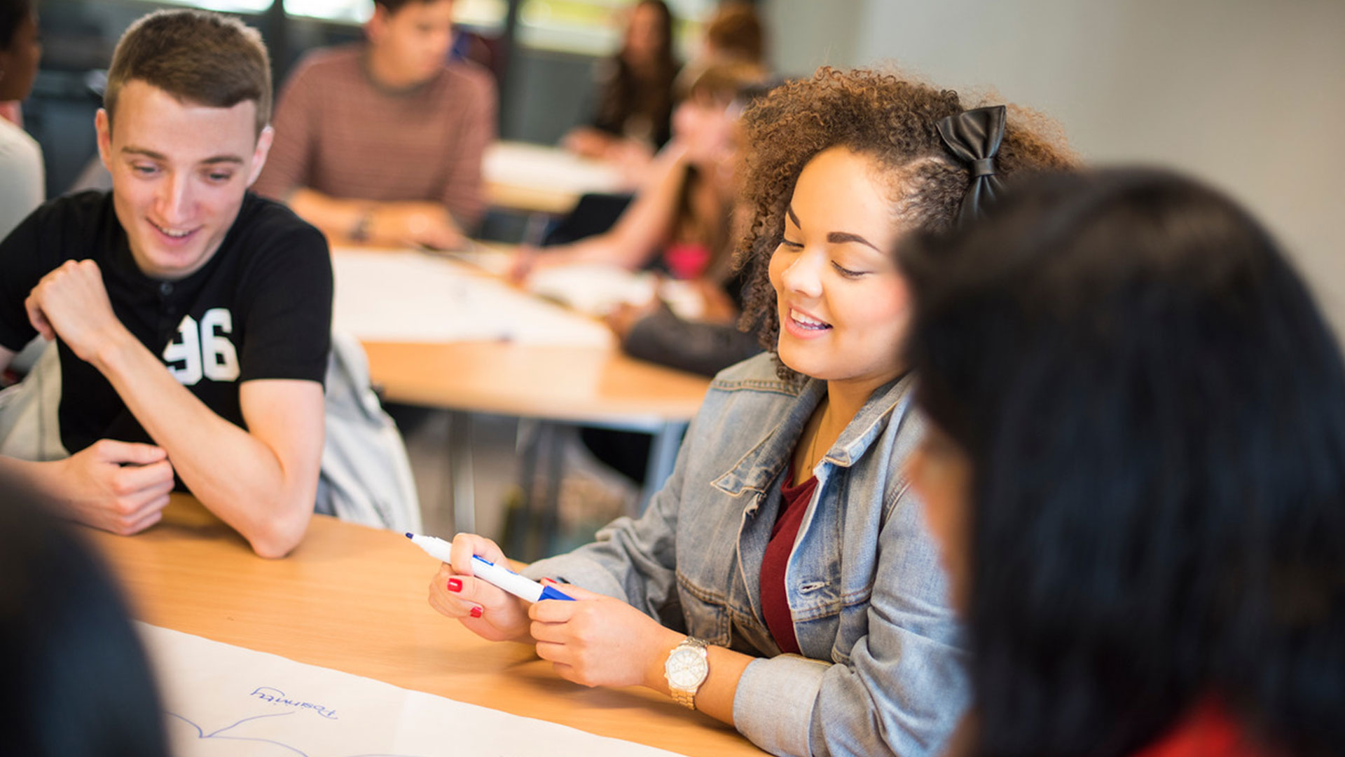 A student smiling whilst working with a small group in a classroom
