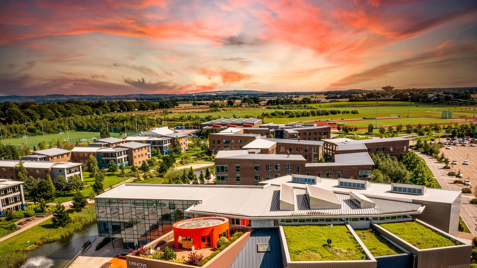 Taken up high by a drone showing Creative Edge with it's grassy roof and the Chancellors halls of residence. A beautiful sunset in the background.