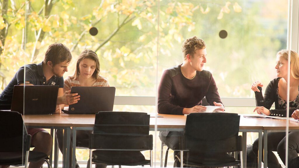 Creative writing students sat in pairs around a table, working on their laptops and taking notes.