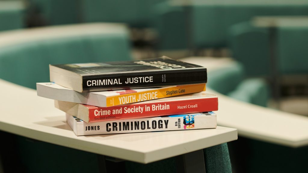 A stack of books on a table with titles on the spines about criminology
