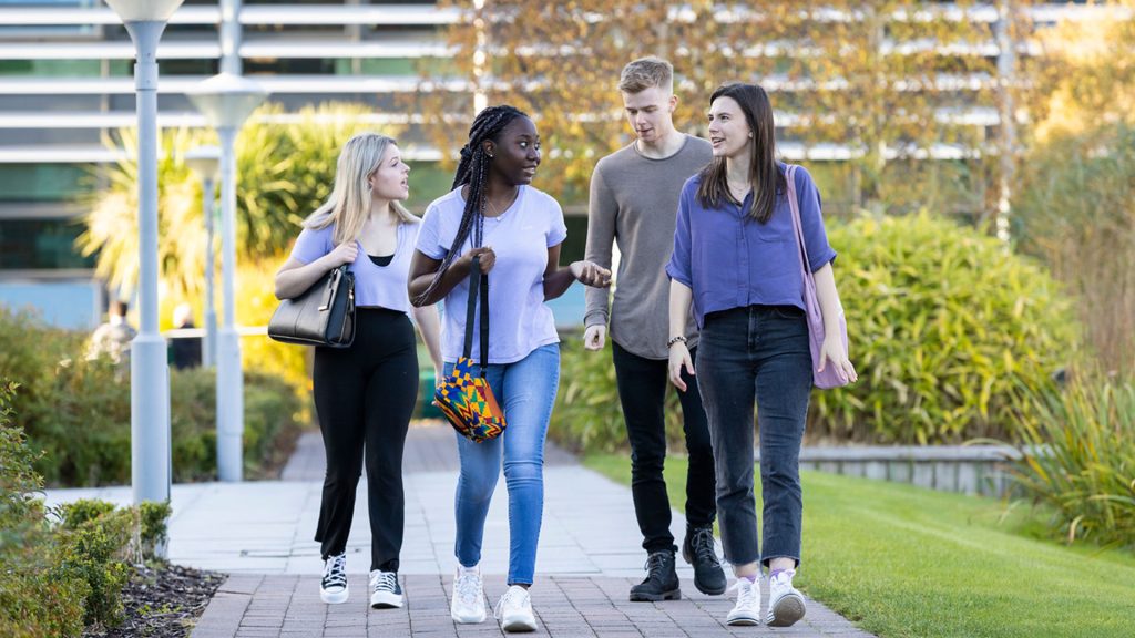 Four students walking through campus together whilst chatting.