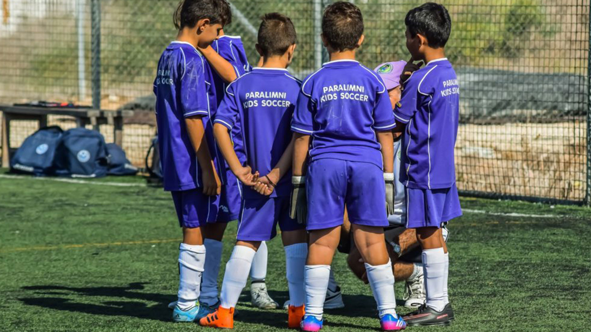 Young children wearing football kits having a huddle on the football pitch