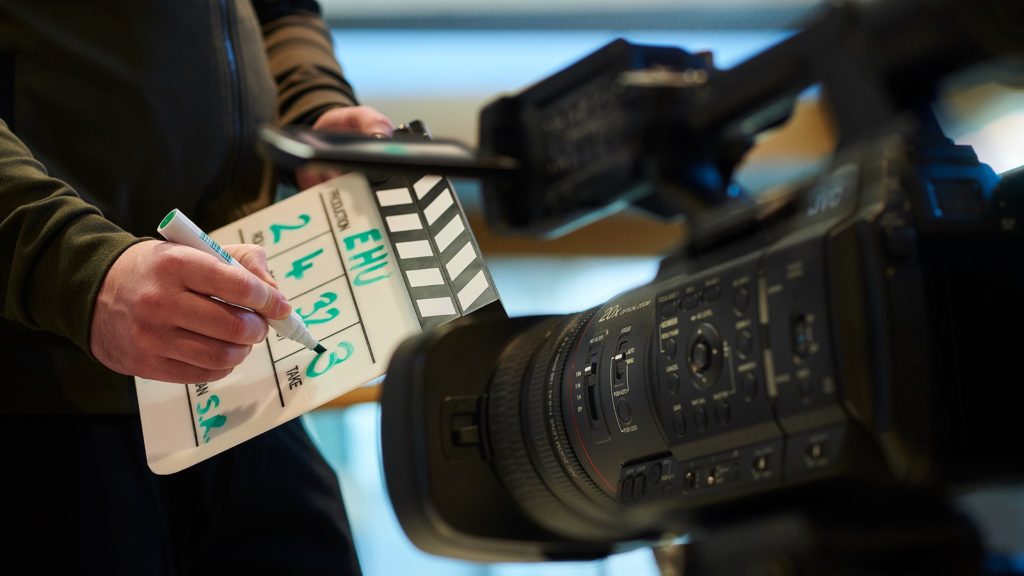 A film student monitors a film camera and holds a clapboard