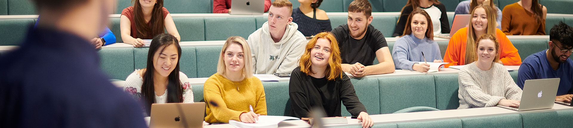Students sitting in a lecture theatre, looking happy and looking at the lecturer