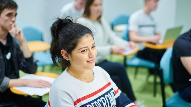 A student sitting at a table listening to a lecturer