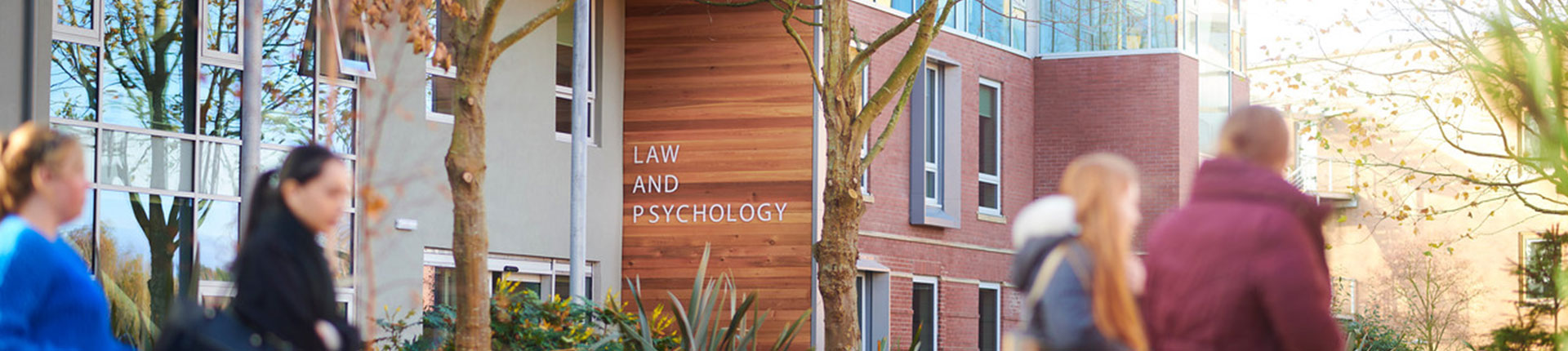 Exterior of the Law and Psychology building. There are four students walking past the building out of focus