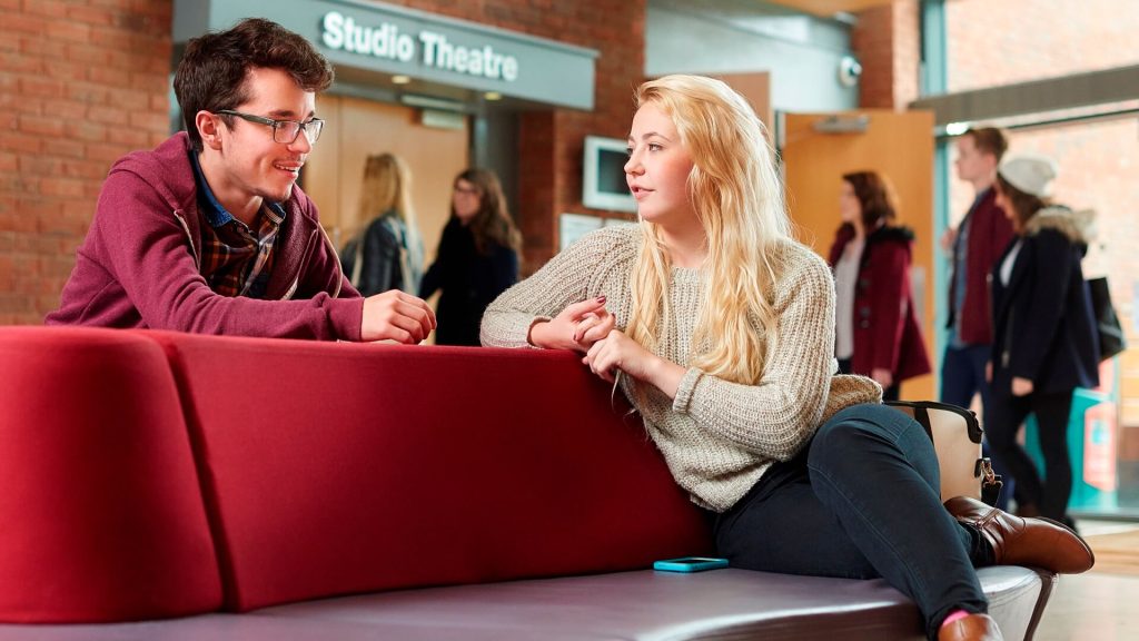 Two students talk in the foyer of the Arts Centre, with the entrance to the Studio Theatre visible behind them.