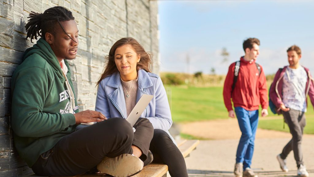 Two students sit on a bench by the Sports Centre overlooking the running track.