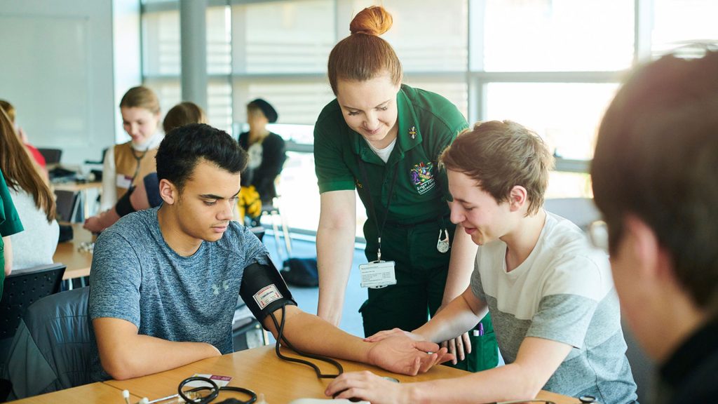 A medical student showing students how to take blood pressure readings at the widening participation event
