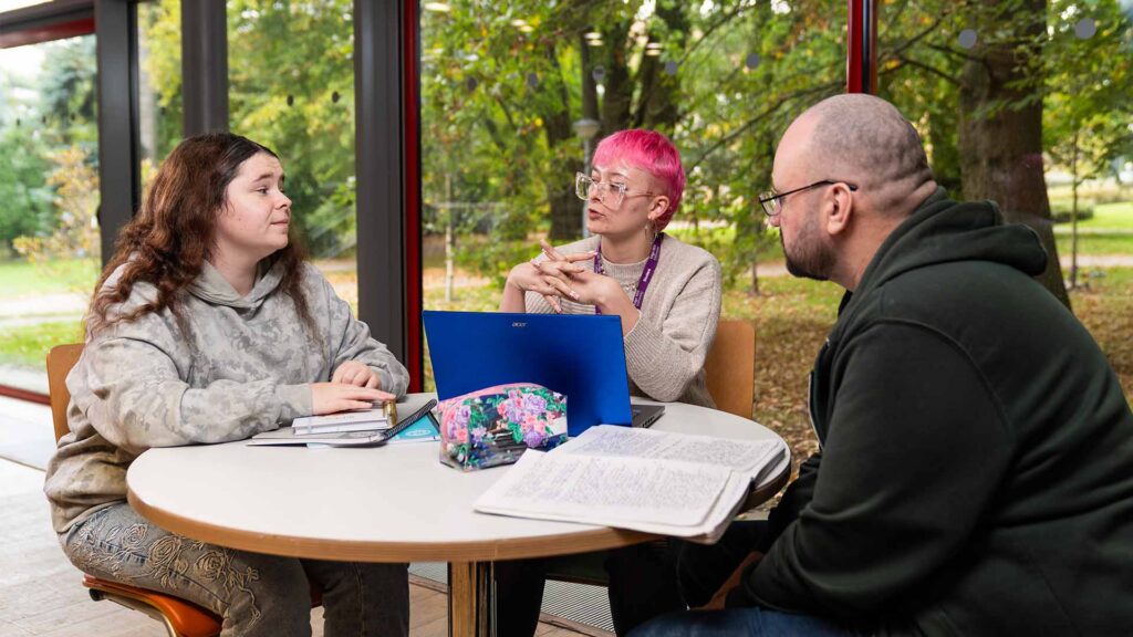 Three students sat around a table with a notepad and laptop