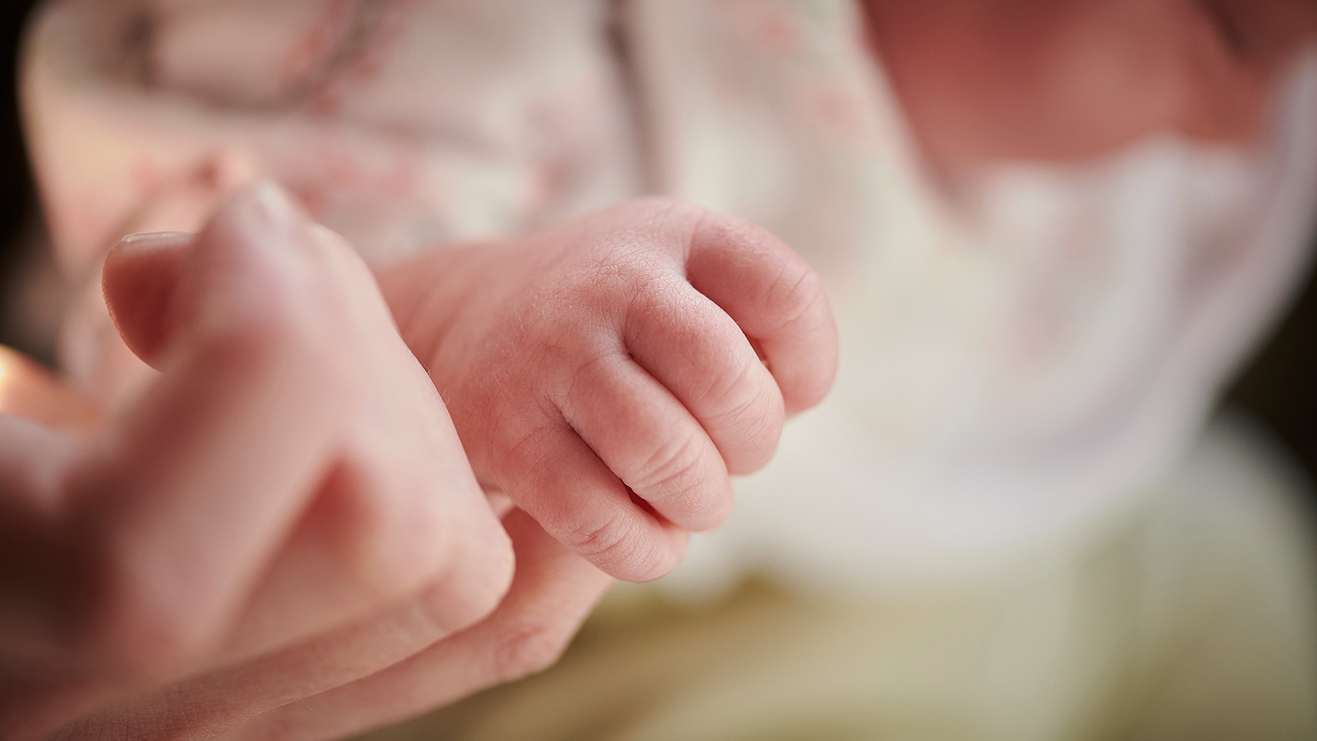 A baby holds a midwife's finger