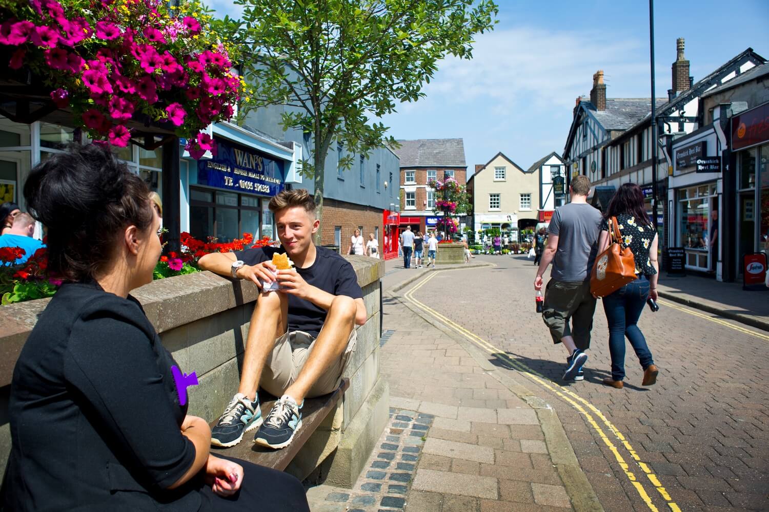 Two students eat lunch on a bench in the centre of Ormskirk.