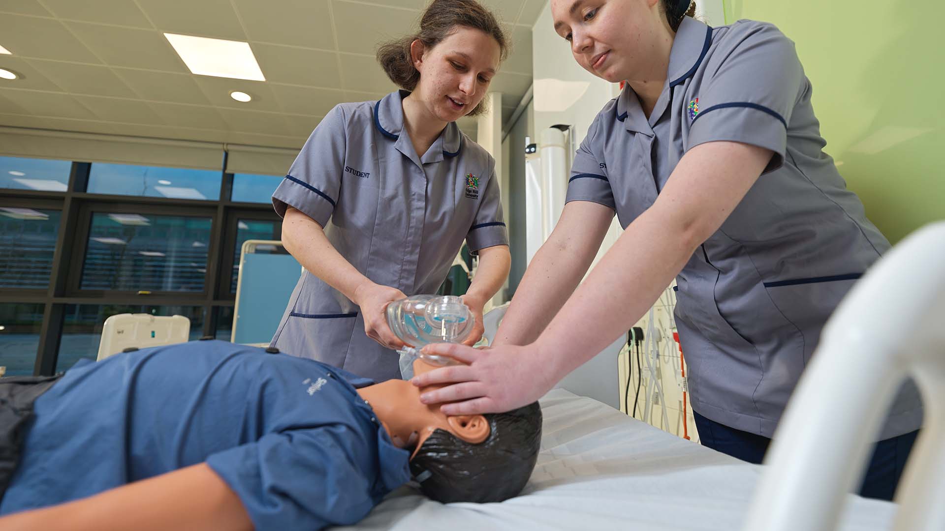 Nursing students in a simulated environment using an oxygen mask on a mannequin