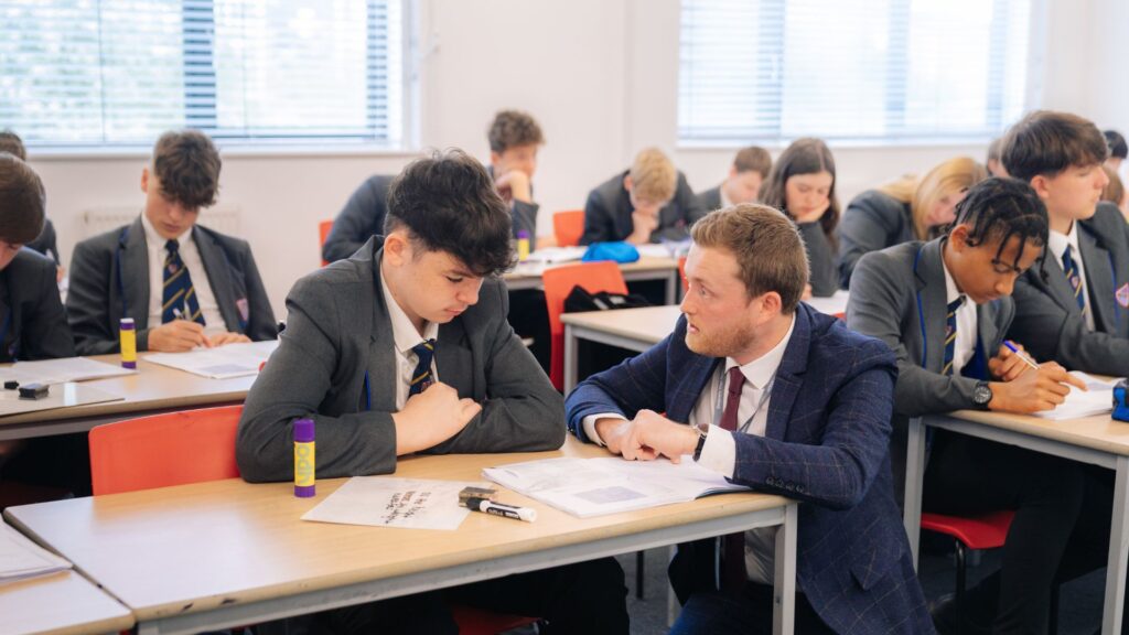classroom of secondary school students with teacher helping a pupil at a table