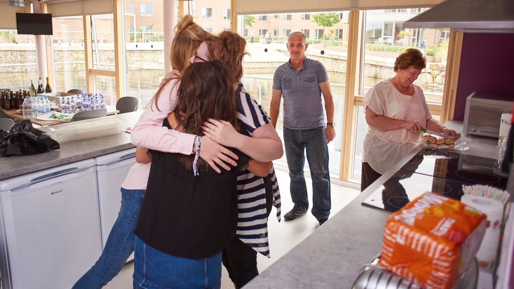 Three students hug whilst two parents look on
