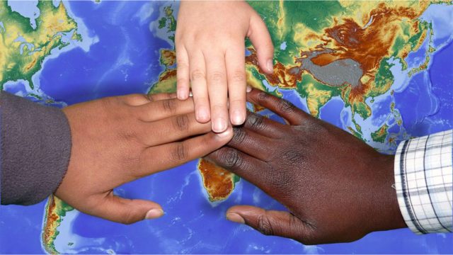 Hands with different skin tones on top of eachother on top of a world map