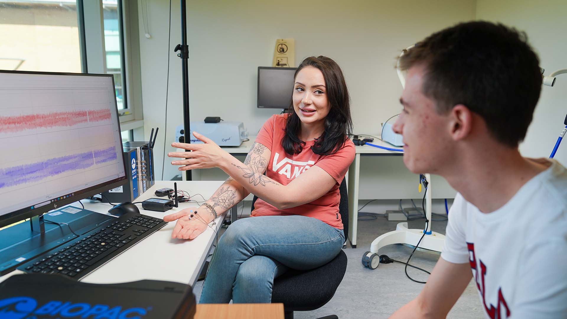 Student discussing brainwave data with a lecturer in a psychology lab while pointing at a computer screen showing EEG signals.