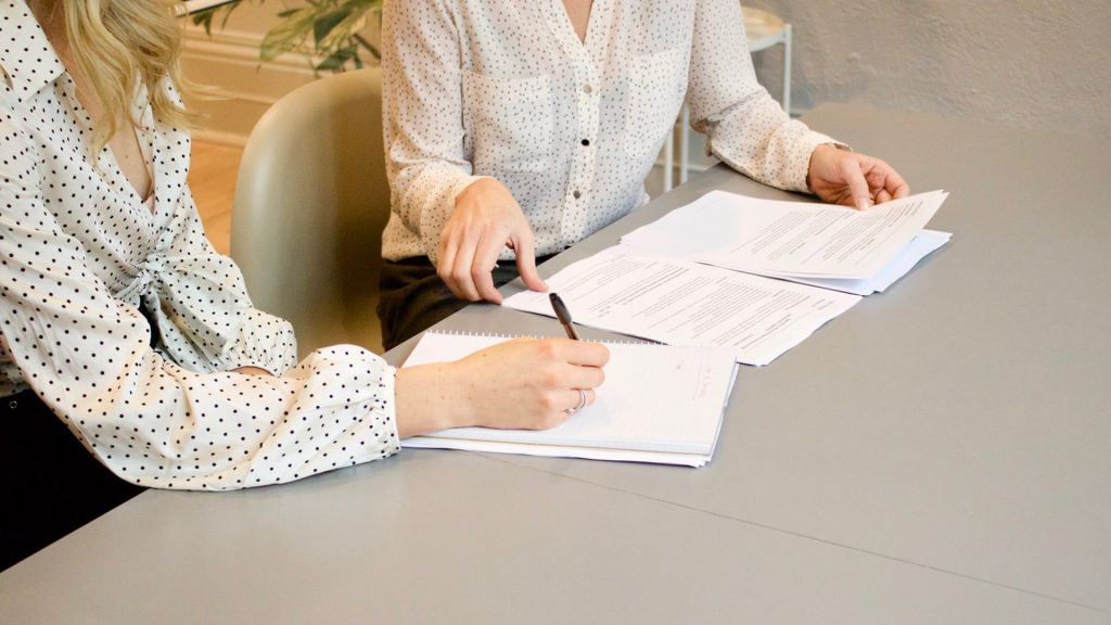 Two colleagues discussing papers and making notes at at a desk together.