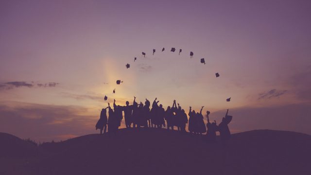 A group of students on a hill at sunset throwing their mortar boards up in the air