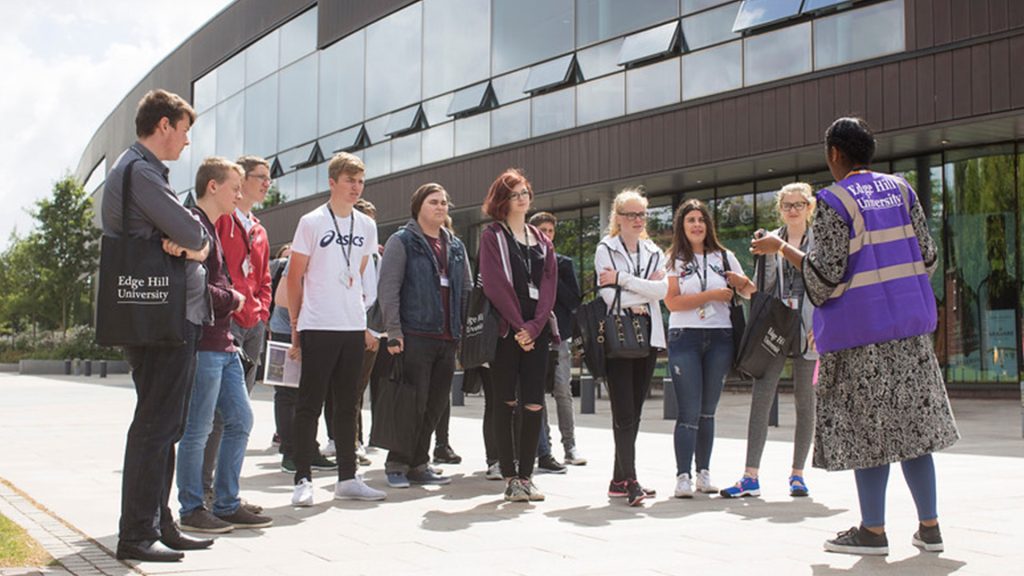 An unrecognisable student guide talking to a group of students outside the Hub