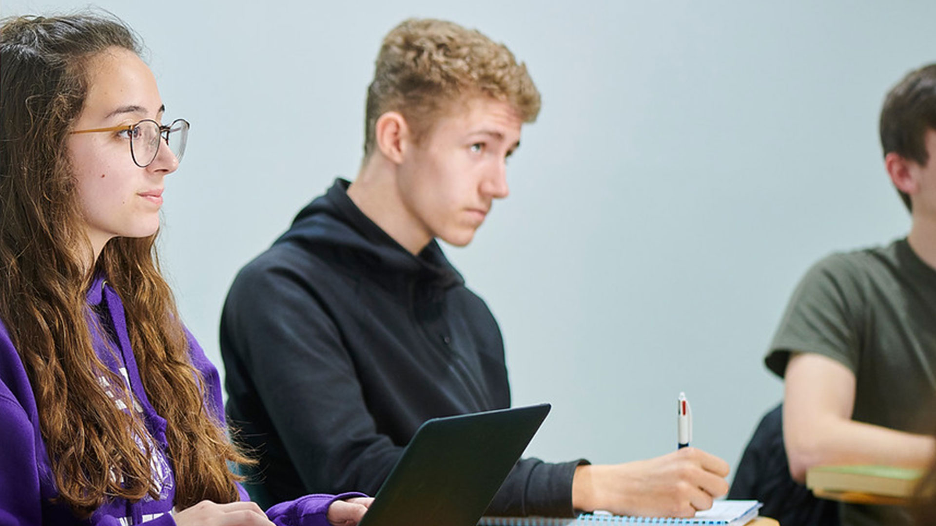 Two students taking notes in a lecture. One of the students is wearing a purple Edge Hill University hoodie.