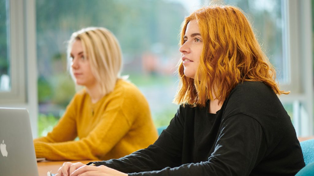 Two students in a class making notes on their laptops.