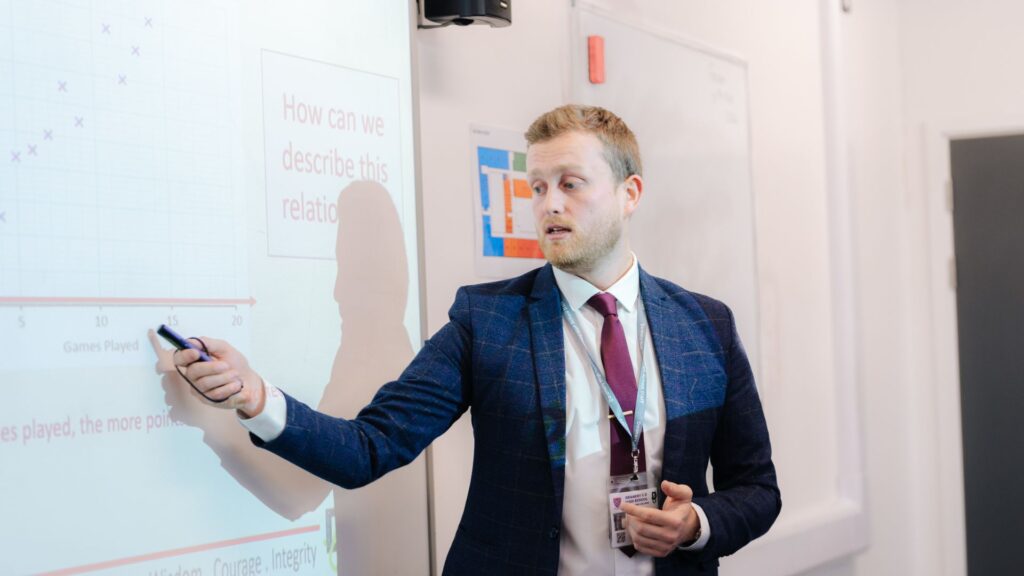Teacher in classroom stood pointing at interactive whiteboard