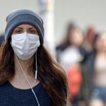 Woman wearing a face mask outside, wearing a hat and headphones