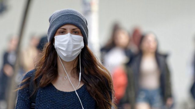 Woman wearing a face mask outside, wearing a hat and headphones