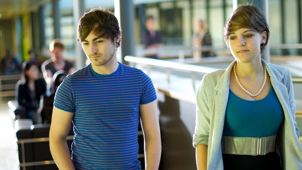 Two students walking through the Business School, with students sat on sofas behind them.