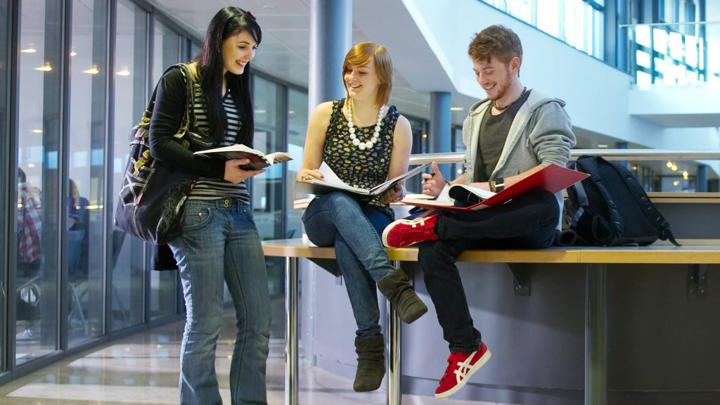 Three students sat in a foyer area comparing notes in their written work.