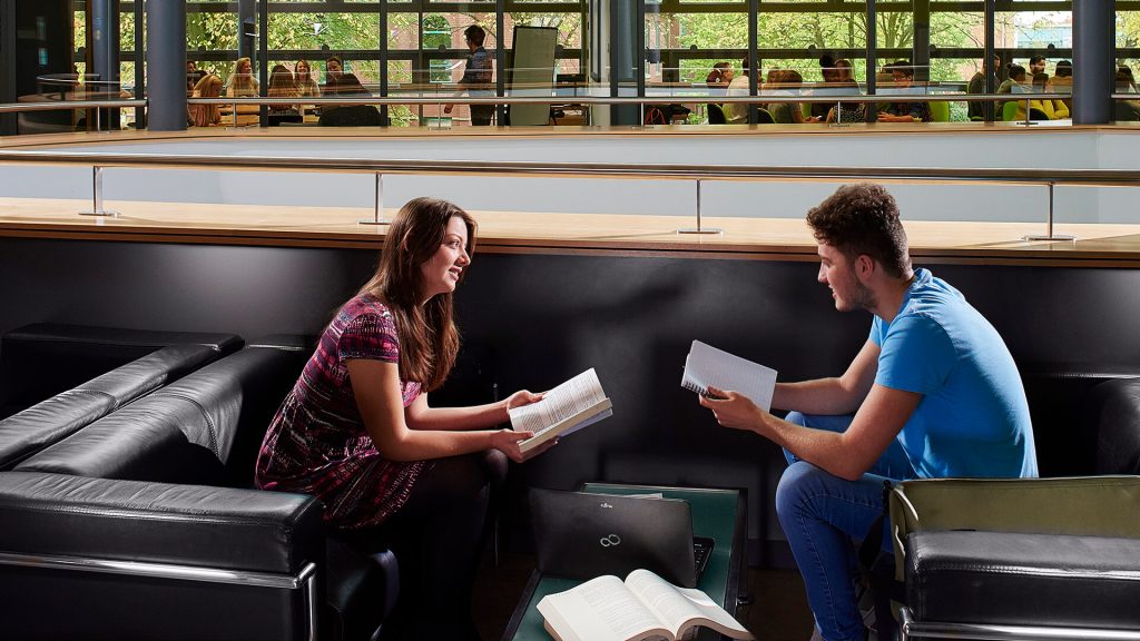 Two students sit on sofas and study in a social learning area in the Business School.