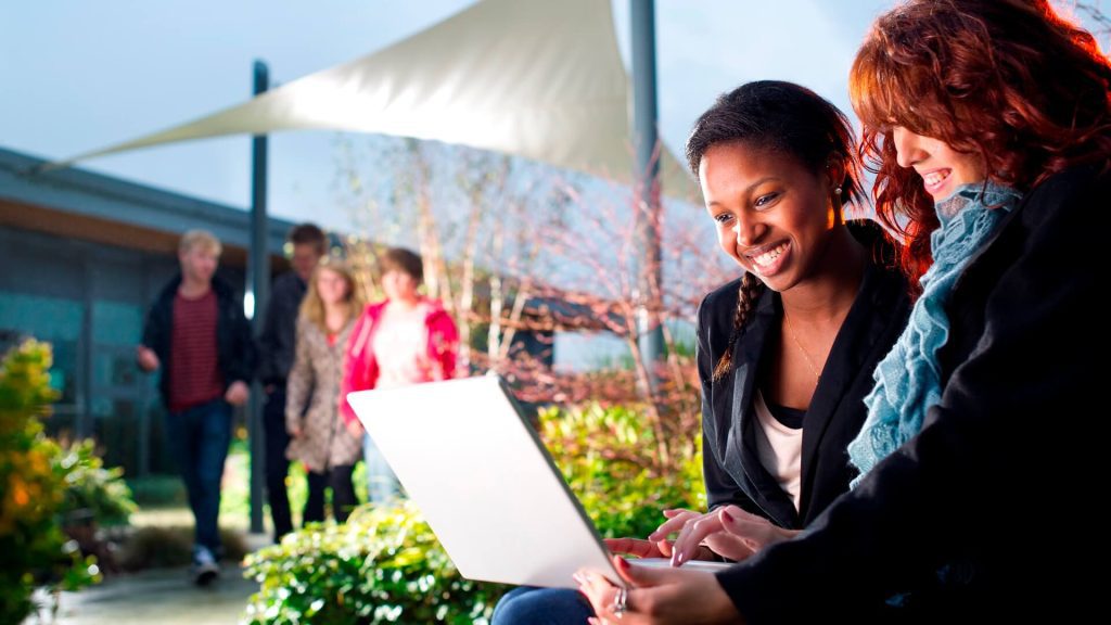 Two students work together, using a laptop, while sitting in the roof garden on top of the Business School.