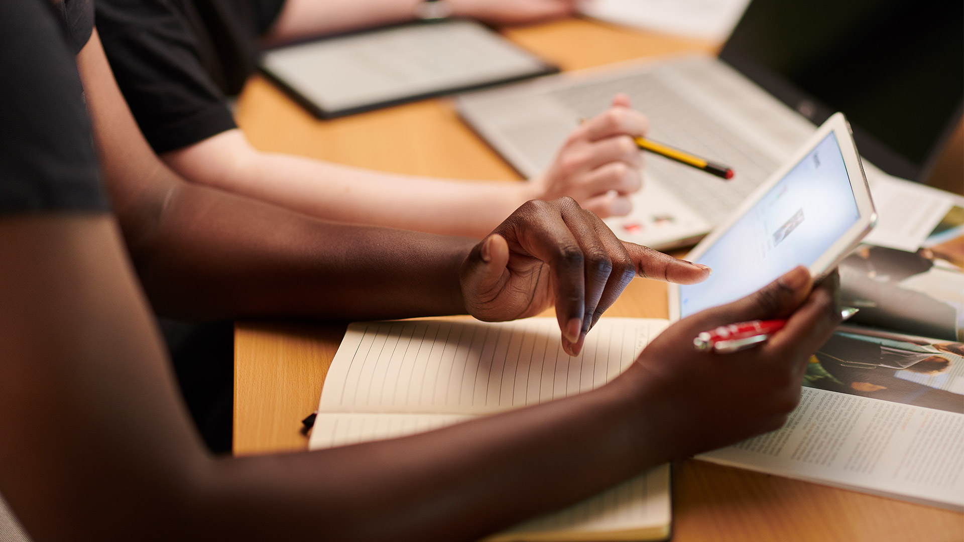 Two people look at a tablet on a table surrounded by papers and documents