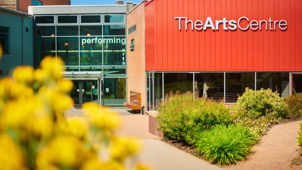 The outside of The Arts Centre. The building is orange and surrounded by plants.