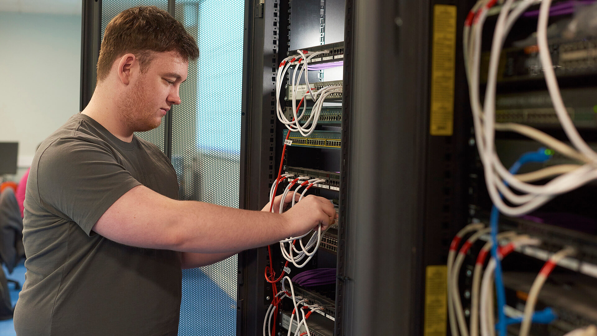 A student plugs wires into the back of a server in a computing laboratory in the Tech Hub.