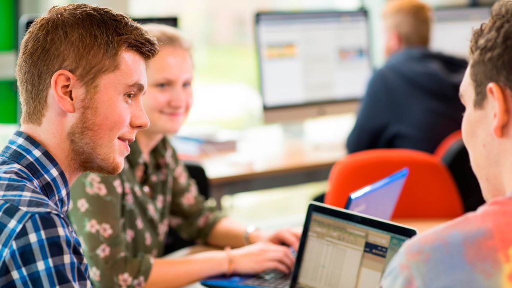 Three students gathered round a laptop study a spreadsheet.