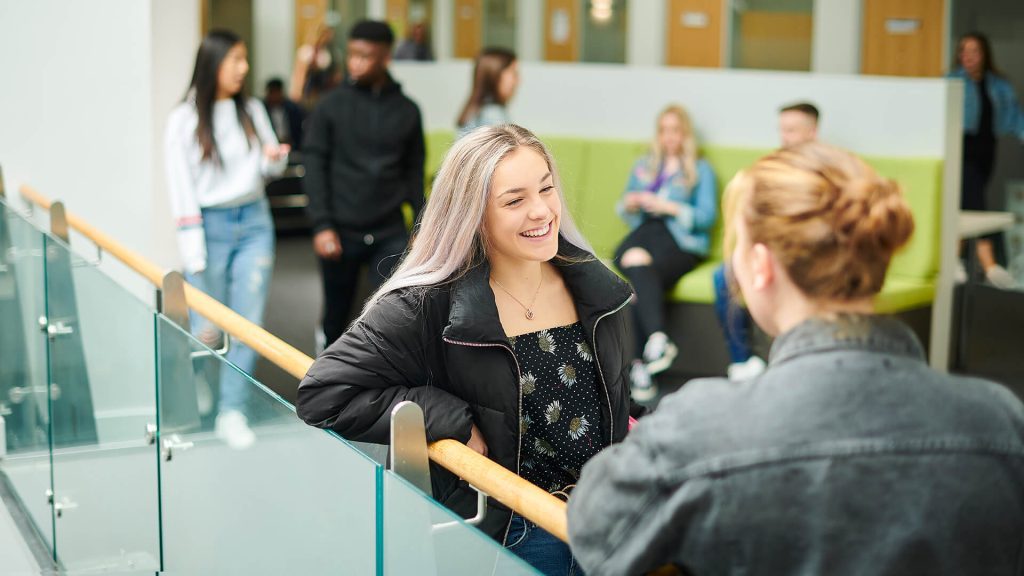 Two students chat while stood near the top of the stairs in the Law and Psychology building.