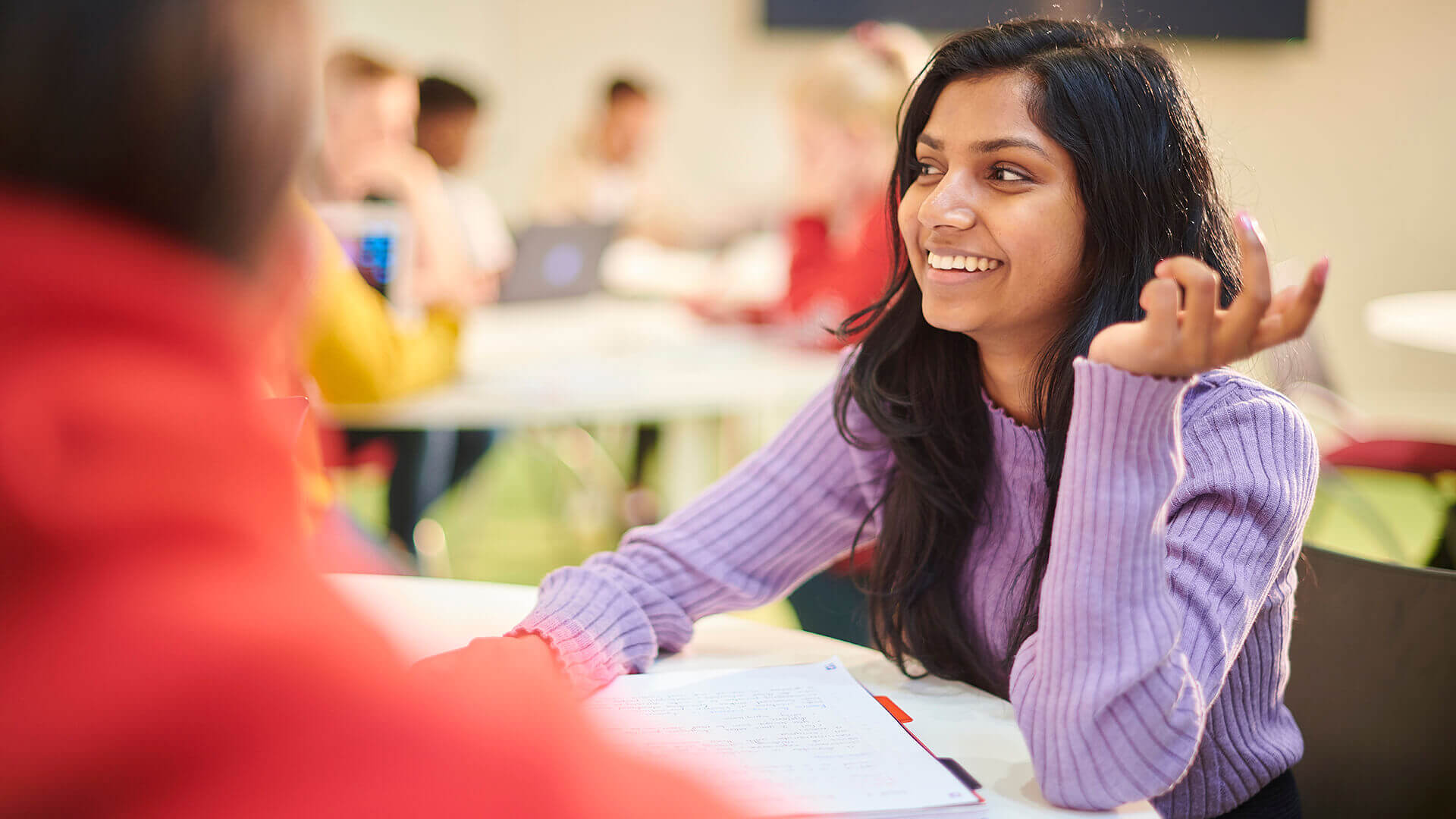 Students engage in discussion while sat round a table during a seminar.