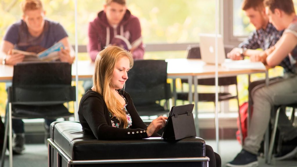 A student uses a tablet while sat on a sofa in a social learning space in Creative Edge.