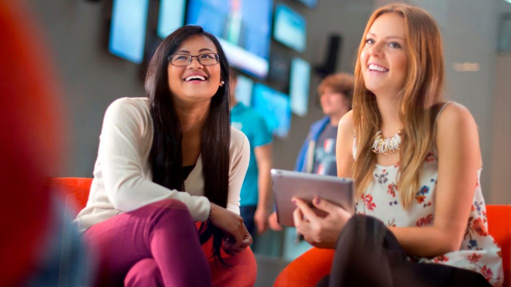 Two students, one holding a tablet, sit in the foyer of the Creative Edge building.