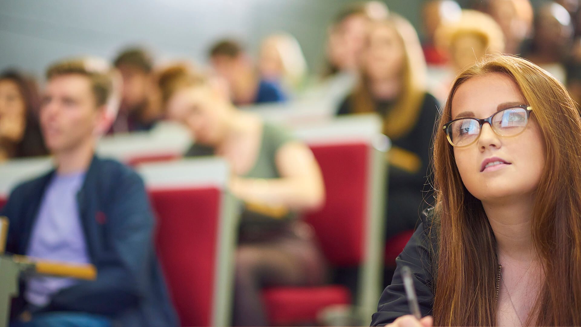 A busy lecture theatre of students making notes and listening to the lecturer addressing them.