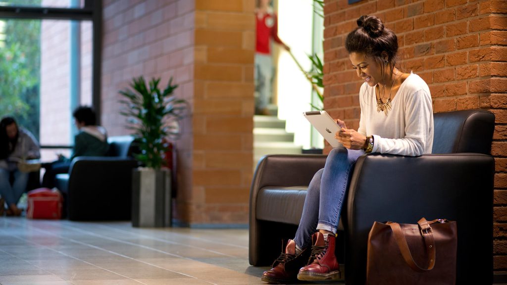 A student studies their iPad while sat on a sofa in the foyer of the Faculty of Education building.