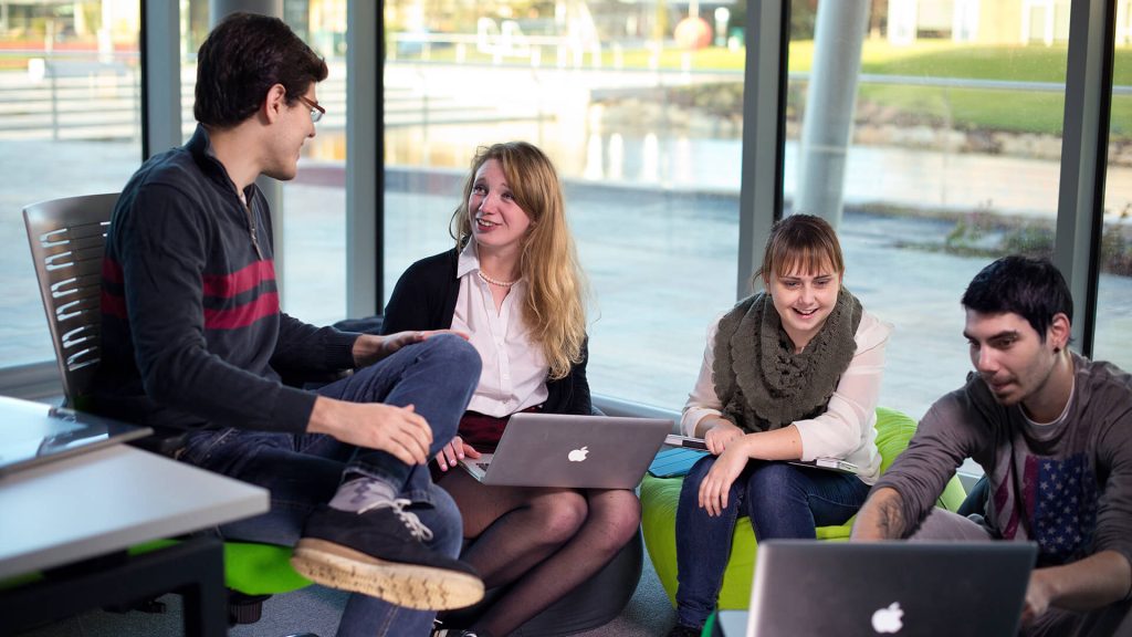 Four students chat and study together while sitting in a classroom in Creative Edge.